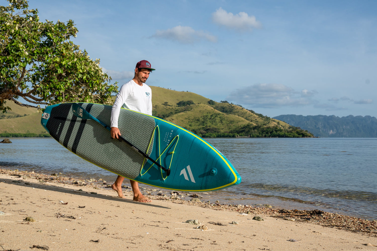 Stand up Paddler geht mit Fanatic Ray air Premium Sup Brett am Strand entlang.