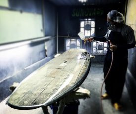Arbeiter beim Lakieren eines Sunova Holz Wave SUP Boards in der Fabrik.