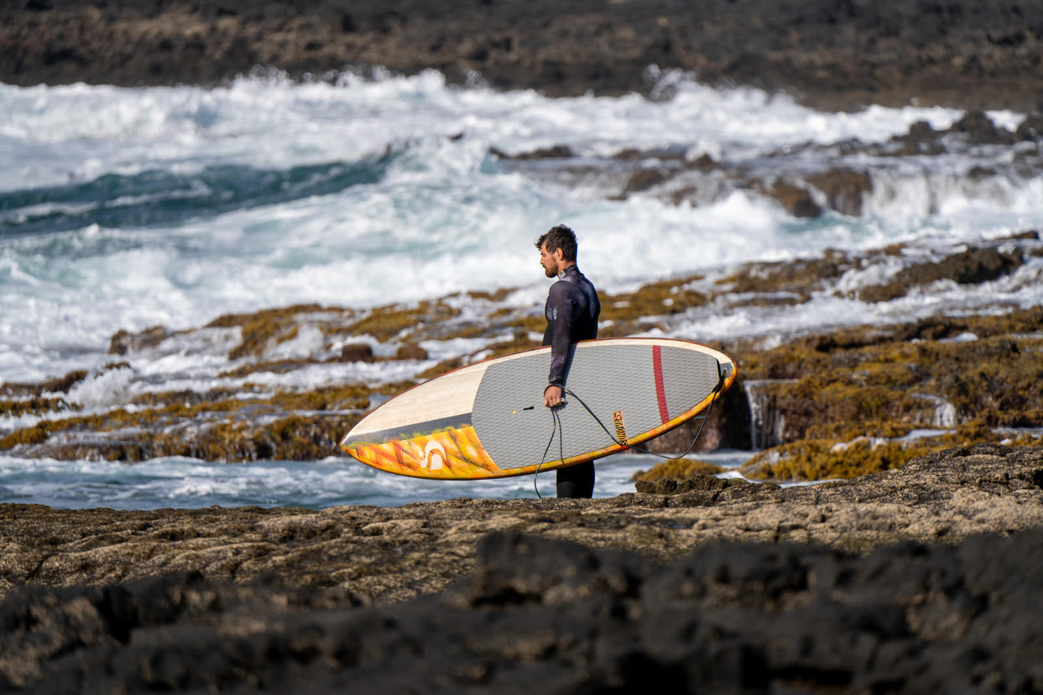 Stand up Paddler der mit dem Sunova Flash Wave SUP Board über die Felsen ins Wasser geht.