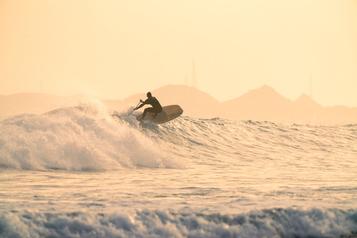 Stand up Paddler mit einem Cutback in die Welle im Sonnenuntergang mit einem Sunova Speeed Wave SUP Board.