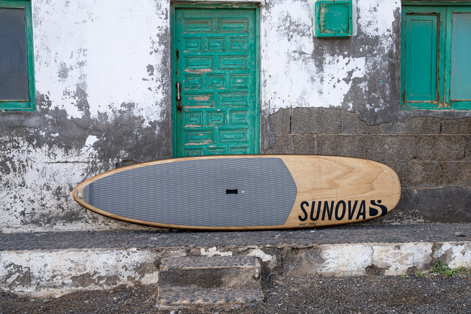 Sunova Style Wave SUP Board auf dem Rail stehend an eine Hauswand angelehnt.