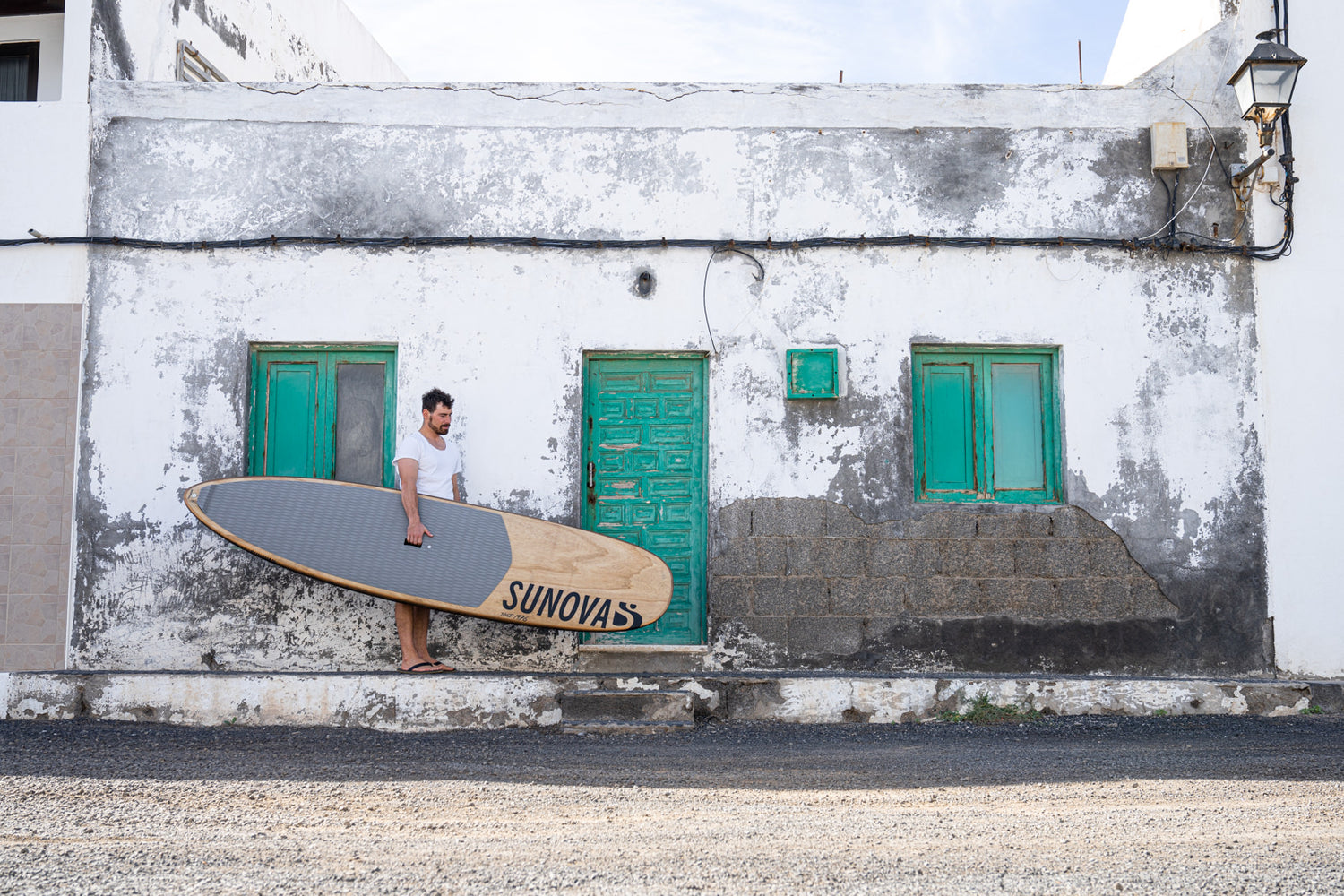Kai-Nicolas Steimer mit dem Sunova Style Wave SUP Board in der Hand vor einer alten Hauswand.